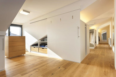 Großes Modernes Ankleidezimmer mit flächenbündigen Schrankfronten, weißen Schränken, hellem Holzboden und braunem Boden in Sonstige