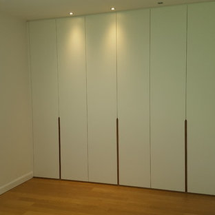 Foto de vestidor unisex, contemporáneo, de tamaño medio, con armarios con paneles lisos, puertas de armario blancas, suelo laminado y suelo marrón