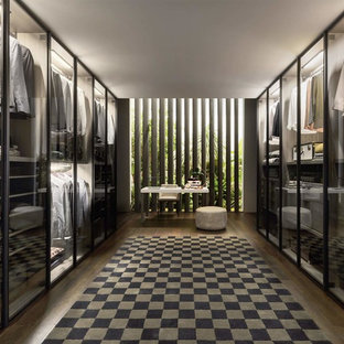 Idee per una grande cabina armadio unisex design con ante di vetro, ante nere, parquet scuro e pavimento marrone