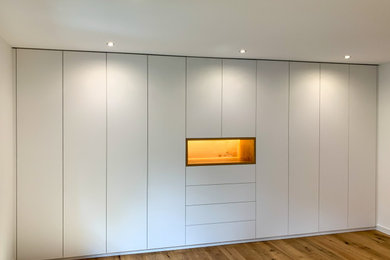 Großes Modernes Ankleidezimmer mit Ankleidebereich, flächenbündigen Schrankfronten, weißen Schränken, braunem Holzboden und braunem Boden in München