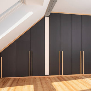 Immagine di una cabina armadio unisex moderna di medie dimensioni con ante lisce, ante nere, parquet chiaro, pavimento marrone e travi a vista