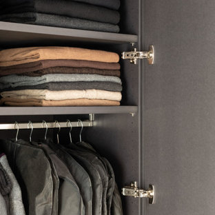 Réalisation d'un dressing minimaliste de taille moyenne et neutre avec un placard à porte plane, des portes de placard noires, un sol en bois clair, un sol marron et un plafond en poutres apparentes.
