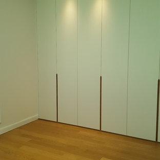 Imagen de vestidor unisex, actual, de tamaño medio, con armarios con paneles lisos, puertas de armario blancas, suelo laminado y suelo marrón