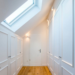 Imagen de armario vestidor unisex, clásico, de tamaño medio, con armarios con rebordes decorativos, puertas de armario blancas, suelo de madera en tonos medios y suelo marrón
