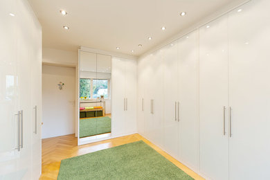 Großer, Neutraler Moderner Begehbarer Kleiderschrank mit flächenbündigen Schrankfronten, weißen Schränken und hellem Holzboden in Essen