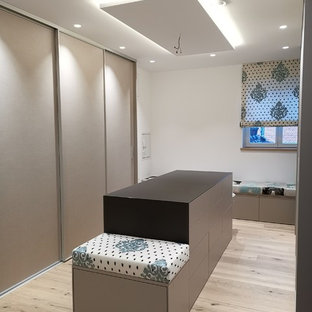 Modelo de vestidor escandinavo, grande, con armarios con paneles lisos, puertas de armario beige y suelo de madera clara