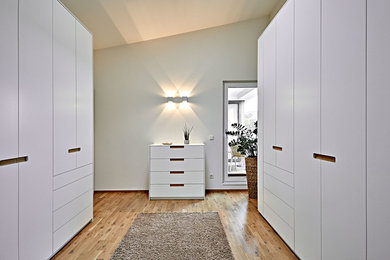 Mittelgroßer, Neutraler Moderner Begehbarer Kleiderschrank mit flächenbündigen Schrankfronten, weißen Schränken, braunem Holzboden und braunem Boden in Sonstige