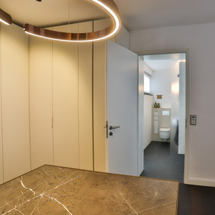 Idées déco pour un grand dressing contemporain neutre avec un placard à porte plane, des portes de placard en bois sombre, un sol en ardoise, un sol noir et un plafond en papier peint.