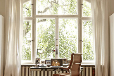 Großes Modernes Arbeitszimmer ohne Kamin mit Arbeitsplatz, freistehendem Schreibtisch, weißer Wandfarbe und braunem Holzboden in Berlin
