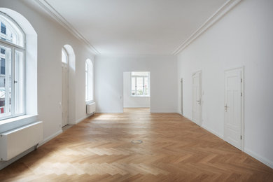 Großes Klassisches Arbeitszimmer ohne Kamin mit Arbeitsplatz, weißer Wandfarbe, hellem Holzboden, freistehendem Schreibtisch und braunem Boden in München