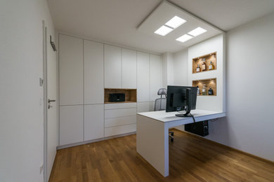 Modernes Arbeitszimmer mit Arbeitsplatz, weißer Wandfarbe, Einbau-Schreibtisch und braunem Boden in München