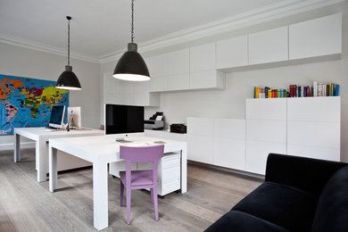 Geräumiges Modernes Arbeitszimmer ohne Kamin mit Arbeitsplatz, grauer Wandfarbe, braunem Holzboden und freistehendem Schreibtisch in Hamburg