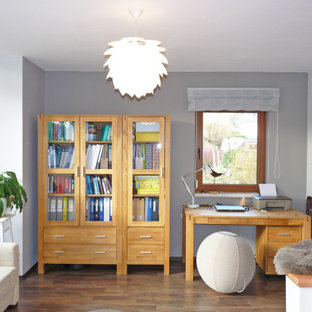 Mittelgroßes Modernes Arbeitszimmer mit Arbeitsplatz, grauer Wandfarbe, braunem Holzboden, Kamin, freistehendem Schreibtisch und braunem Boden in Dresden