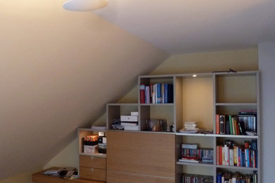 Modelo de despacho actual de tamaño medio con biblioteca, paredes beige, suelo de madera pintada y escritorio empotrado