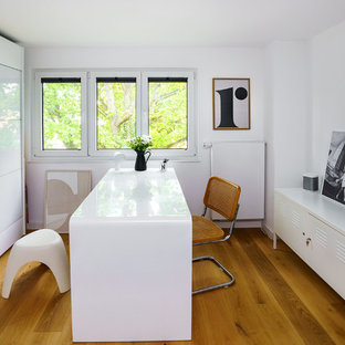 Großes Modernes Arbeitszimmer ohne Kamin mit Arbeitsplatz, weißer Wandfarbe, braunem Holzboden, freistehendem Schreibtisch und braunem Boden in Frankfurt am Main