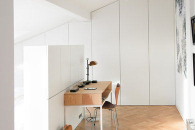 Mittelgroßes Modernes Arbeitszimmer ohne Kamin mit weißer Wandfarbe, braunem Holzboden, braunem Boden, Arbeitsplatz und freistehendem Schreibtisch in Berlin