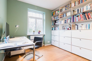 Mittelgroßes Modernes Arbeitszimmer mit Arbeitsplatz, grüner Wandfarbe, braunem Holzboden und freistehendem Schreibtisch in Frankfurt am Main