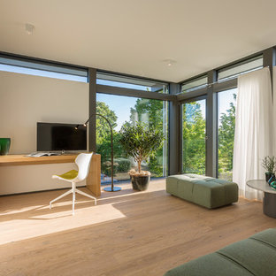 Großes Modernes Arbeitszimmer mit weißer Wandfarbe, hellem Holzboden, freistehendem Schreibtisch und beigem Boden in Sonstige