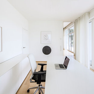 Mittelgroßes Modernes Arbeitszimmer ohne Kamin mit Arbeitsplatz, weißer Wandfarbe, hellem Holzboden, freistehendem Schreibtisch und beigem Boden in Köln