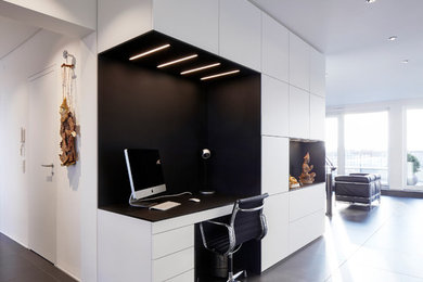 На фото: рабочее место среднего размера в стиле модернизм с белыми стенами, встроенным рабочим столом и черным полом без камина с