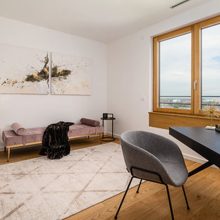 Mittelgroßes Modernes Arbeitszimmer ohne Kamin mit Arbeitsplatz, weißer Wandfarbe, braunem Holzboden, freistehendem Schreibtisch und braunem Boden in München