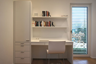 Kleines Modernes Arbeitszimmer mit Arbeitsplatz, weißer Wandfarbe, hellem Holzboden, Einbau-Schreibtisch und braunem Boden in Düsseldorf
