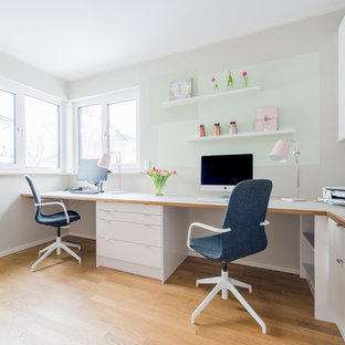 Großes Nordisches Arbeitszimmer ohne Kamin mit Arbeitsplatz, beiger Wandfarbe, braunem Holzboden, Einbau-Schreibtisch und braunem Boden in Berlin