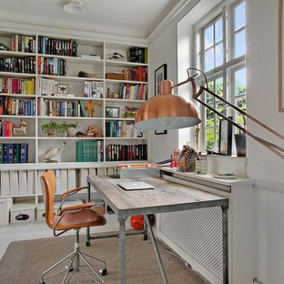 Bild på ett mellanstort skandinaviskt hemmabibliotek, med vita väggar, målat trägolv och ett fristående skrivbord