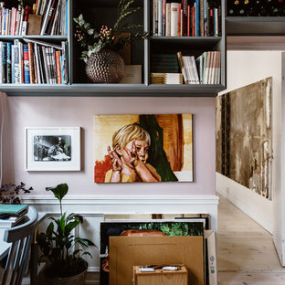 Bild på ett eklektiskt hemmabibliotek, med rosa väggar, ljust trägolv, ett fristående skrivbord och beiget golv