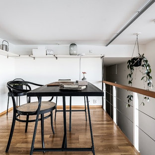 Bild på ett minimalistiskt arbetsrum, med vita väggar, mellanmörkt trägolv, ett fristående skrivbord och brunt golv