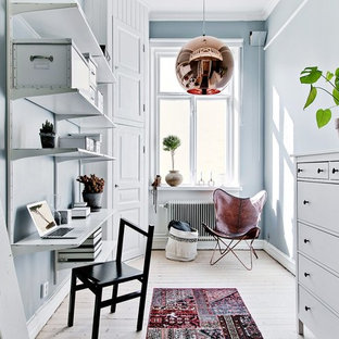 Minimalistisk inredning av ett litet hemmabibliotek, med blå väggar, ljust trägolv, beiget golv och ett inbyggt skrivbord