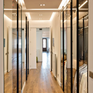 Immagine di una grande cabina armadio unisex contemporanea con ante di vetro, pavimento in legno massello medio e pavimento marrone