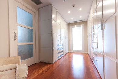 Modelo de armario vestidor unisex clásico renovado grande con armarios con paneles lisos, puertas de armario blancas y suelo de madera en tonos medios