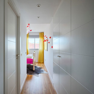 Imagen de armario vestidor unisex, bohemio, grande, con armarios con paneles con relieve, puertas de armario blancas y suelo de madera en tonos medios