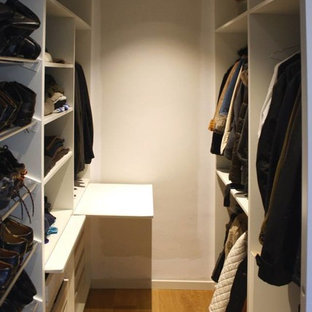 Imagen de armario vestidor unisex, nórdico, de tamaño medio, con armarios abiertos, puertas de armario blancas y suelo de madera en tonos medios