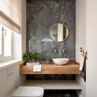 Esempio di un bagno di servizio nordico di medie dimensioni con nessun'anta, ante in legno chiaro, WC sospeso, piastrelle grigie, piastrelle in gres porcellanato, pareti beige, pavimento in gres porcellanato, lavabo a bacinella, top in legno, pavimento grigio e top marrone