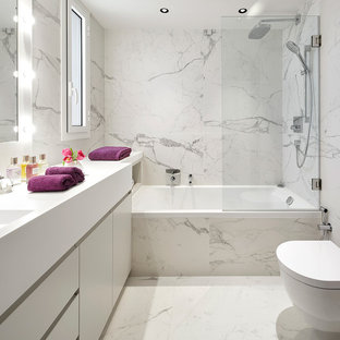 Modelo de aseo contemporáneo con armarios con paneles lisos, puertas de armario blancas, baldosas y/o azulejos blancos, paredes blancas, lavabo integrado, suelo blanco, encimeras blancas y sanitario de pared