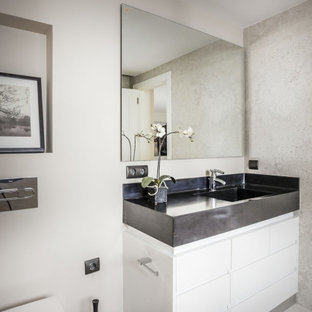 Foto de aseo contemporáneo con armarios con paneles lisos, puertas de armario blancas, sanitario de pared, paredes blancas, suelo gris y encimeras negras