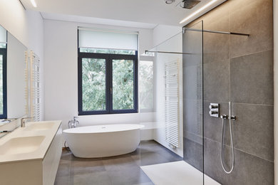 Diseño de cuarto de baño moderno con armarios con paneles lisos, puertas de armario blancas, baldosas y/o azulejos grises, paredes grises, suelo gris y encimeras blancas