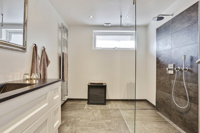 This is an example of a large traditional ensuite bathroom in Copenhagen with raised-panel cabinets, white cabinets, a built-in shower, grey tiles, stone tiles, white walls, ceramic flooring, an integrated sink, laminate worktops and an open shower.