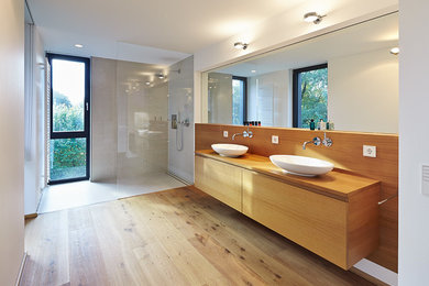 デュッセルドルフにある広いコンテンポラリースタイルのおしゃれなバスルーム (浴槽なし) (中間色木目調キャビネット、オープン型シャワー、白い壁、無垢フローリング、ベッセル式洗面器) の写真