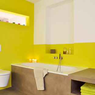 Foto di una stanza da bagno contemporanea con nessun'anta, ante marroni, vasca da incasso, WC sospeso e pareti gialle