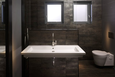 Diseño de cuarto de baño contemporáneo con lavabo suspendido, ducha a ras de suelo, sanitario de pared, baldosas y/o azulejos marrones, paredes grises y aseo y ducha