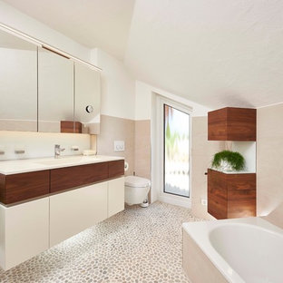 Mittelgroßes Modernes Duschbad mit flächenbündigen Schrankfronten, Einbaubadewanne, beigefarbenen Fliesen, weißer Wandfarbe, Kiesel-Bodenfliesen, integriertem Waschbecken, beigem Boden, weißen Schränken, Wandtoilette und weißer Waschtischplatte in Stuttgart