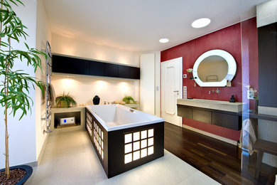 Asiatisches Duschbad mit braunen Schränken, freistehender Badewanne, Wandtoilette, weißer Wandfarbe, braunem Holzboden und Trogwaschbecken in Berlin