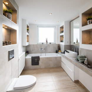 Mittelgroßes Modernes Duschbad mit flächenbündigen Schrankfronten, weißen Schränken, Einbaubadewanne, bodengleicher Dusche, Wandtoilette, grauen Fliesen, Keramikfliesen, weißer Wandfarbe, Keramikboden, integriertem Waschbecken, gefliestem Waschtisch, braunem Boden, Falttür-Duschabtrennung und grauer Waschtischplatte in Hannover