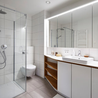 Kleines Nordisches Duschbad mit flächenbündigen Schrankfronten, weißen Schränken, Eckdusche, Wandtoilette, weißen Fliesen, Travertinfliesen, weißer Wandfarbe, Einbauwaschbecken, beigem Boden, Falttür-Duschabtrennung und weißer Waschtischplatte in Stuttgart