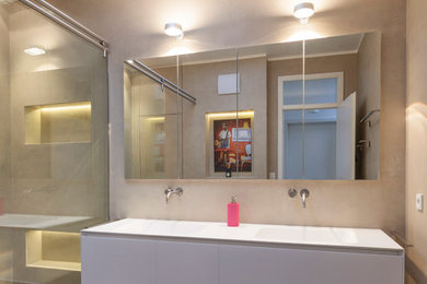 Bild på ett mellanstort funkis badrum med dusch, med släta luckor, vita skåp, en kantlös dusch, beige väggar, ett integrerad handfat, grått golv och dusch med skjutdörr