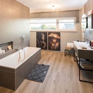 Modernes Badezimmer mit flächenbündigen Schrankfronten, schwarzen Schränken, Einbaubadewanne, braunem Holzboden, integriertem Waschbecken, braunem Boden und weißer Waschtischplatte in Sonstige