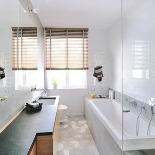Kleines Modernes Duschbad mit flächenbündigen Schrankfronten, bodengleicher Dusche, Wandtoilette, weißer Wandfarbe, Waschtisch aus Holz, grauem Boden, Falttür-Duschabtrennung, grauer Waschtischplatte, hellbraunen Holzschränken, Einbaubadewanne, grauen Fliesen und Unterbauwaschbecken in München